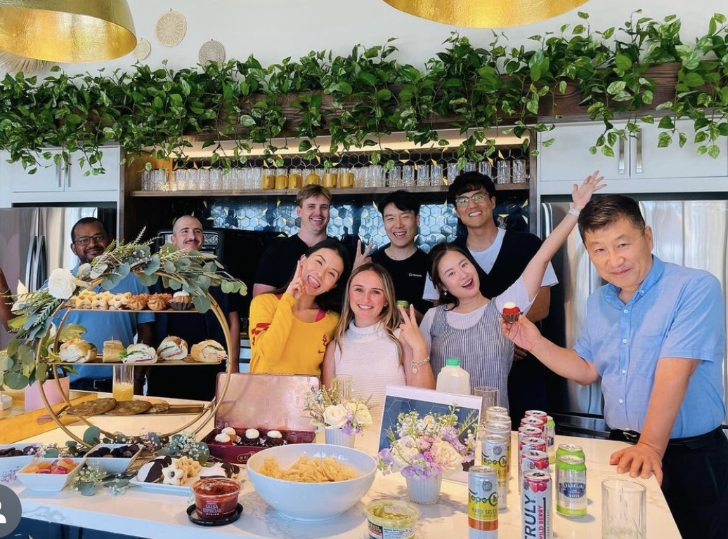 Group of people posing for the camera at an event; there is food and drinks out on the counter