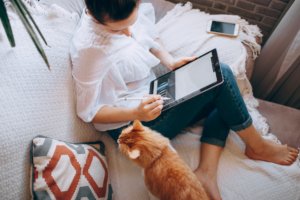 A woman sitting on her couch with a tablet and pet cat next to her